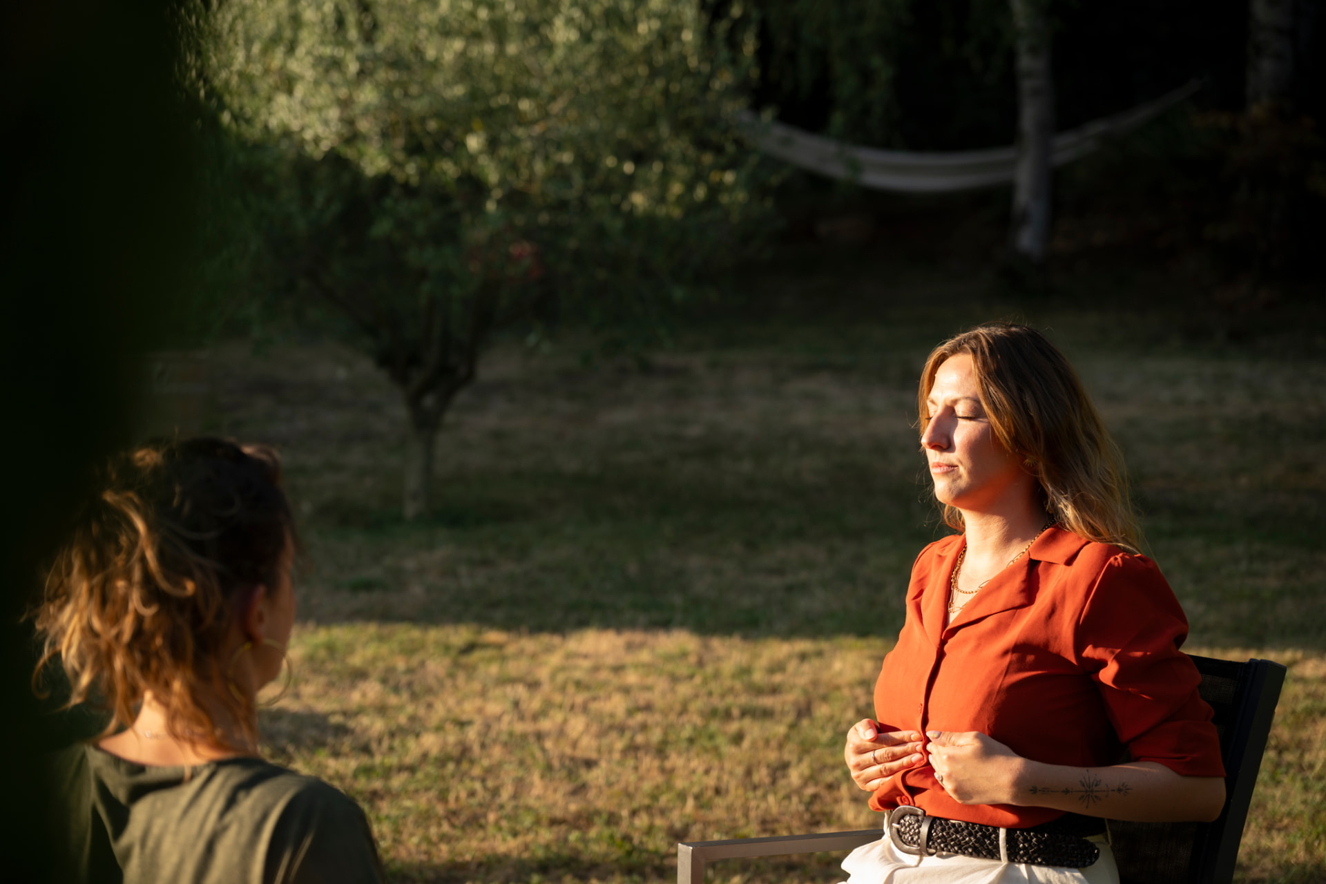 Séance de sophrologie en extérieur : Camille, les yeux fermés et une main sur le ventre, pratique un exercice de respiration au calme dans un jardin